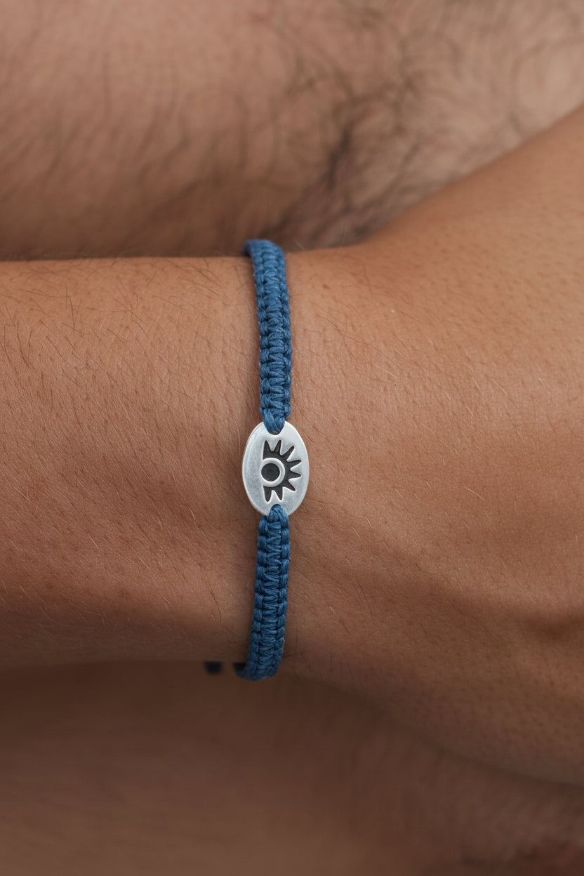 Blue braided bracelet with a silver charm on a wrist against a brown background