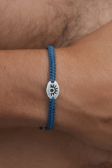 Blue braided bracelet with a silver charm on a wrist against a brown background